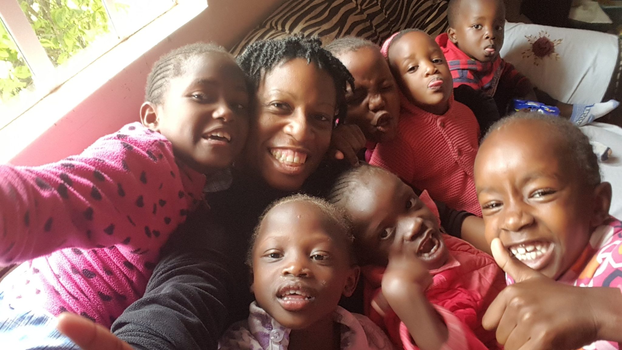Kennesha smiling for a group selfie with Ivy, Cynthia, Hadassah, Esther, and other children inside Nissi House in Kenya in 2018.