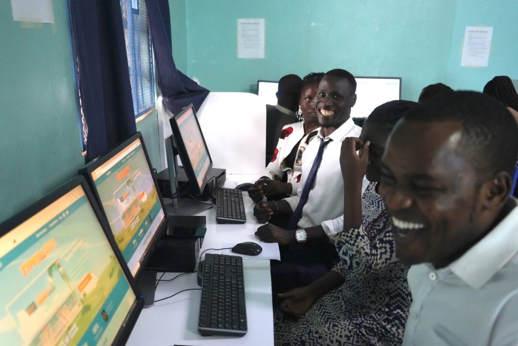 Adults sit at computer workstations while a man in a white shirt and tie smiles toward the camera.