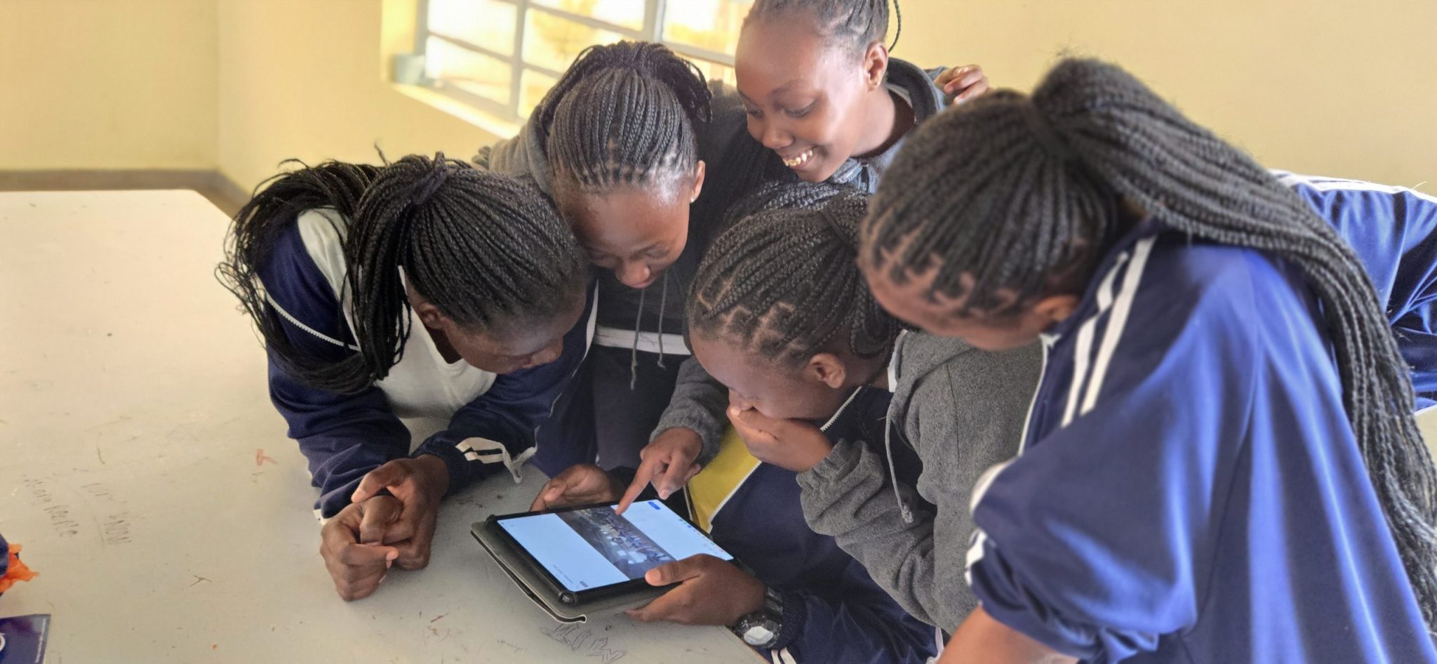 Students gathered around a tablet watching something together at Faith Premier High School.