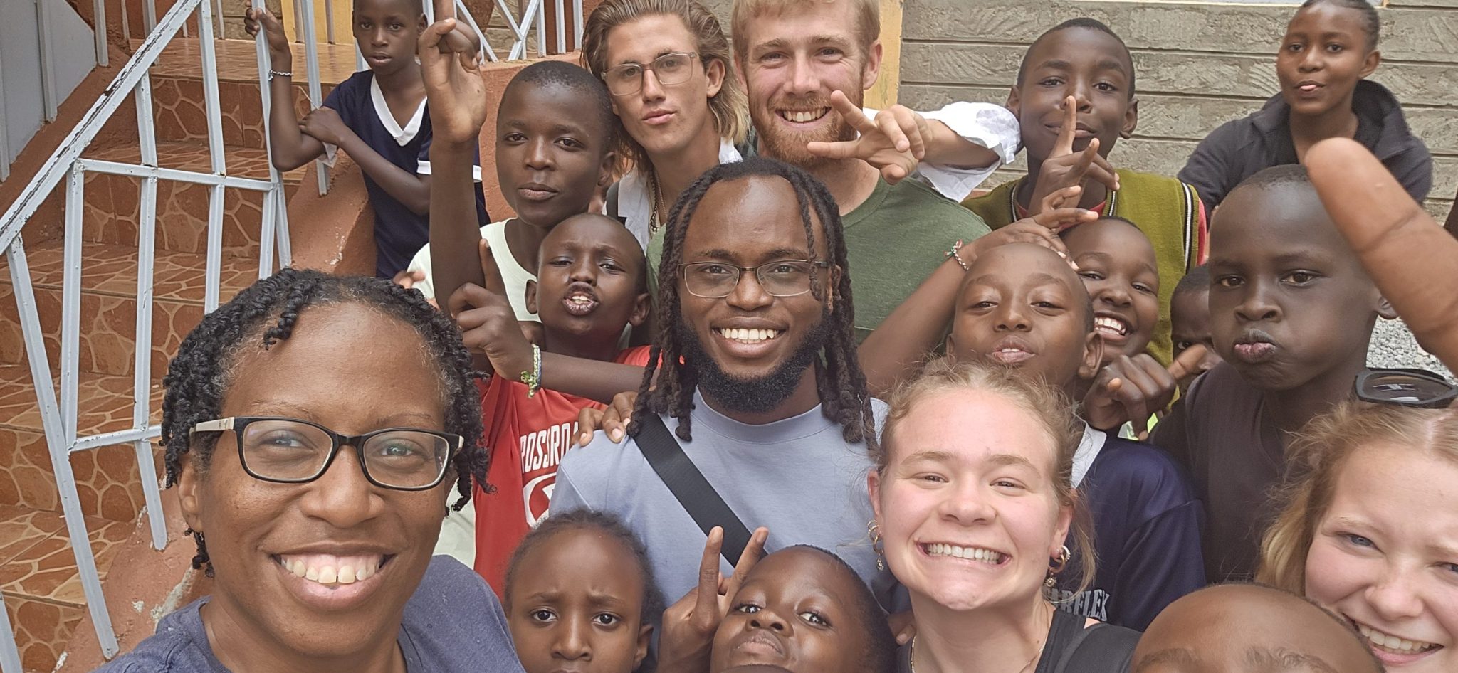 Volunteers and children crowd together for a large outdoor group selfie at Happy Life.