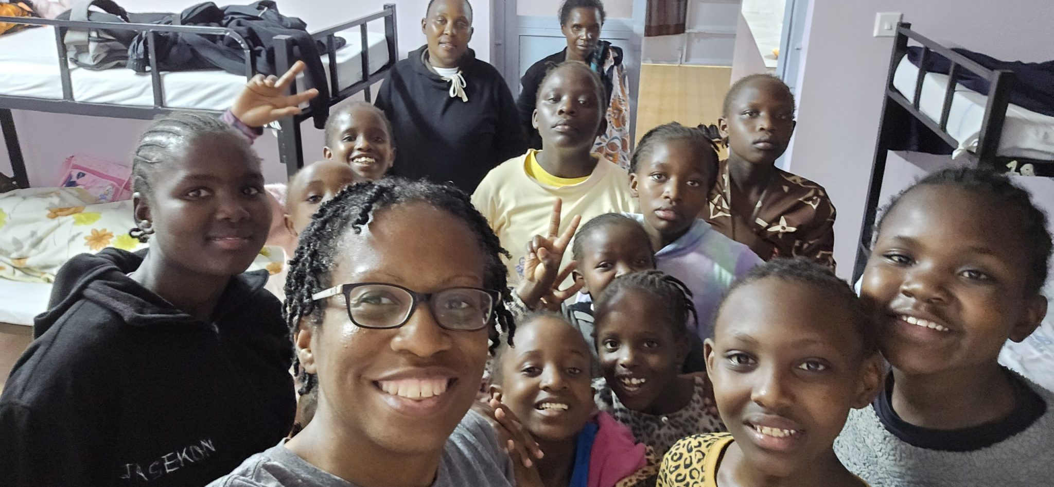 Kennesha taking a group selfie with girls and caregivers inside a Happy Life dormitory room.