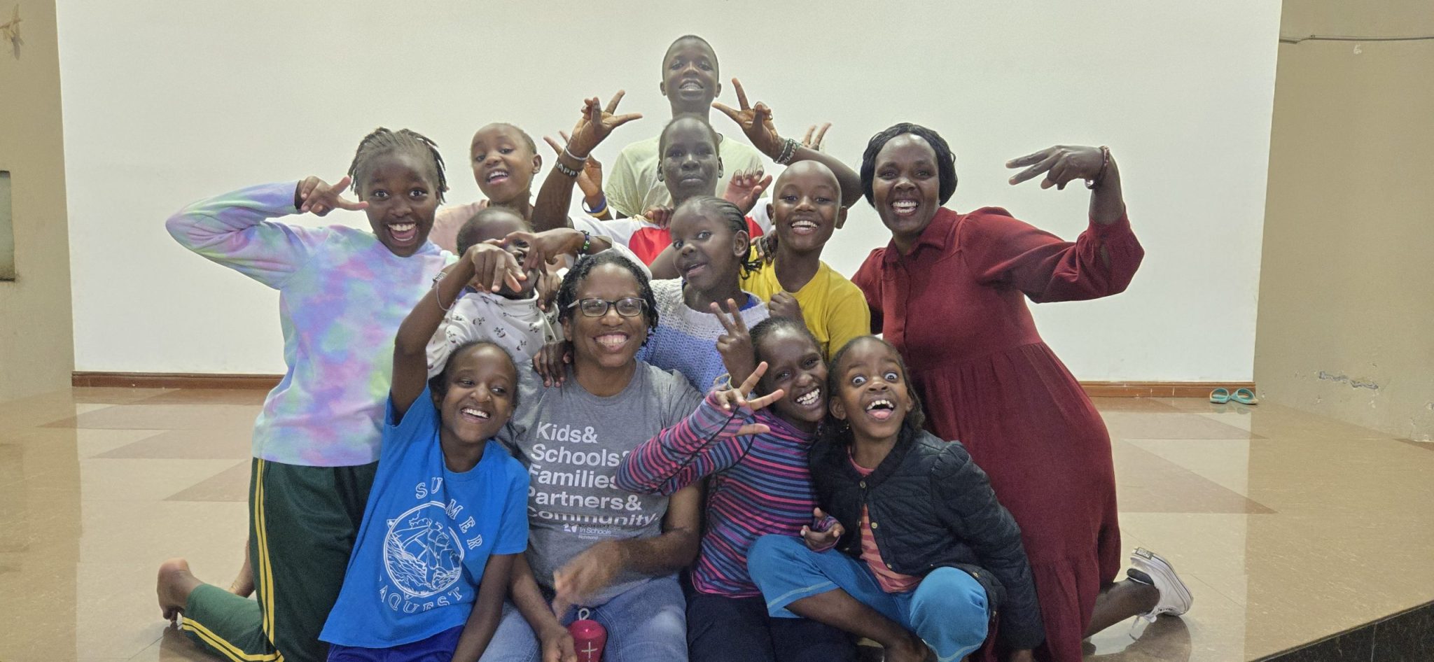 Kennesha  surrounded by a joyful group of children and another adult during a gathering at Happy Life in Juja Farm.