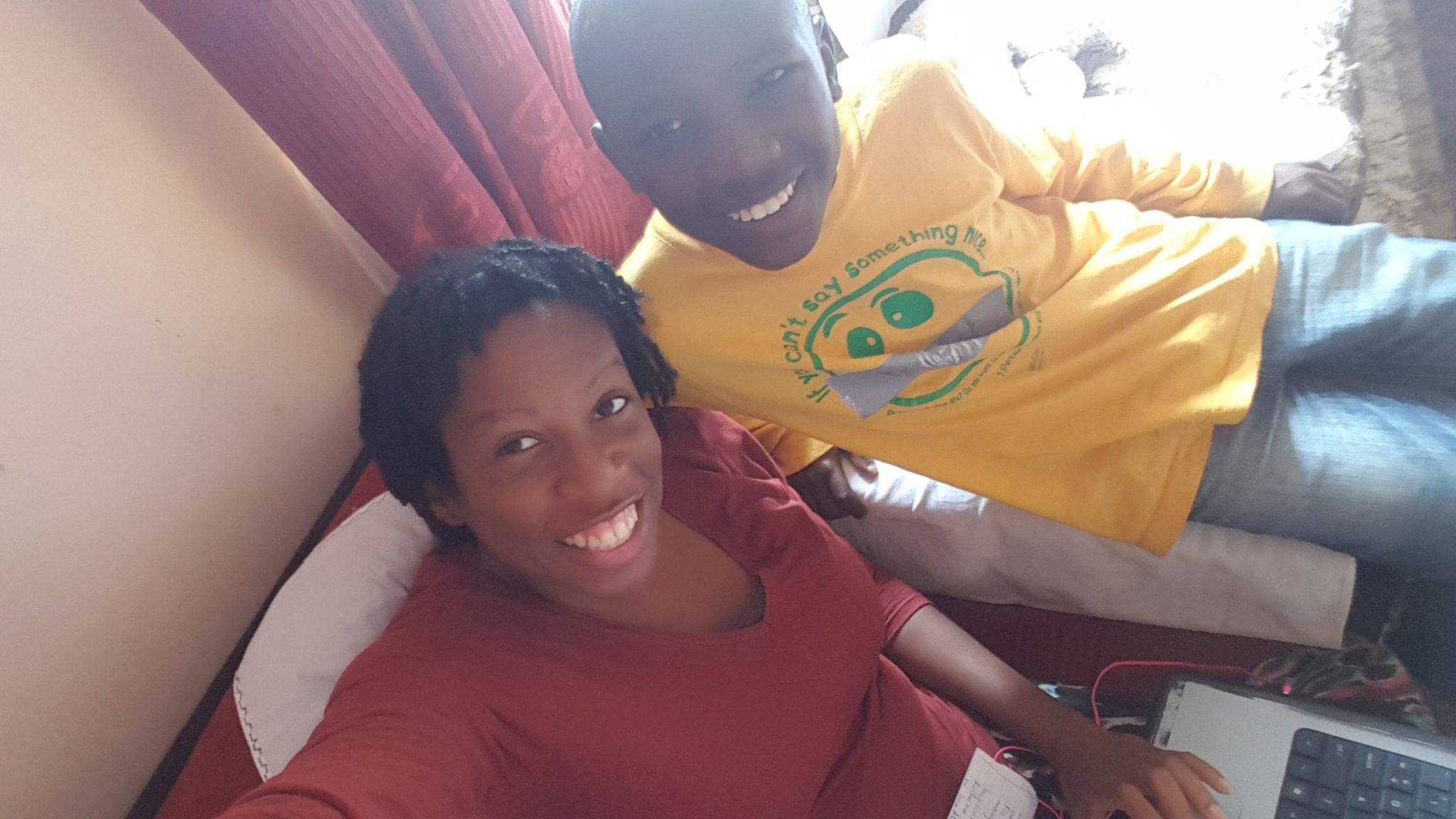 Kennesha smiling beside Peter in a yellow shirt while seated near a laptop at Happy Life in Juja Farm, Kenya, in 2018.