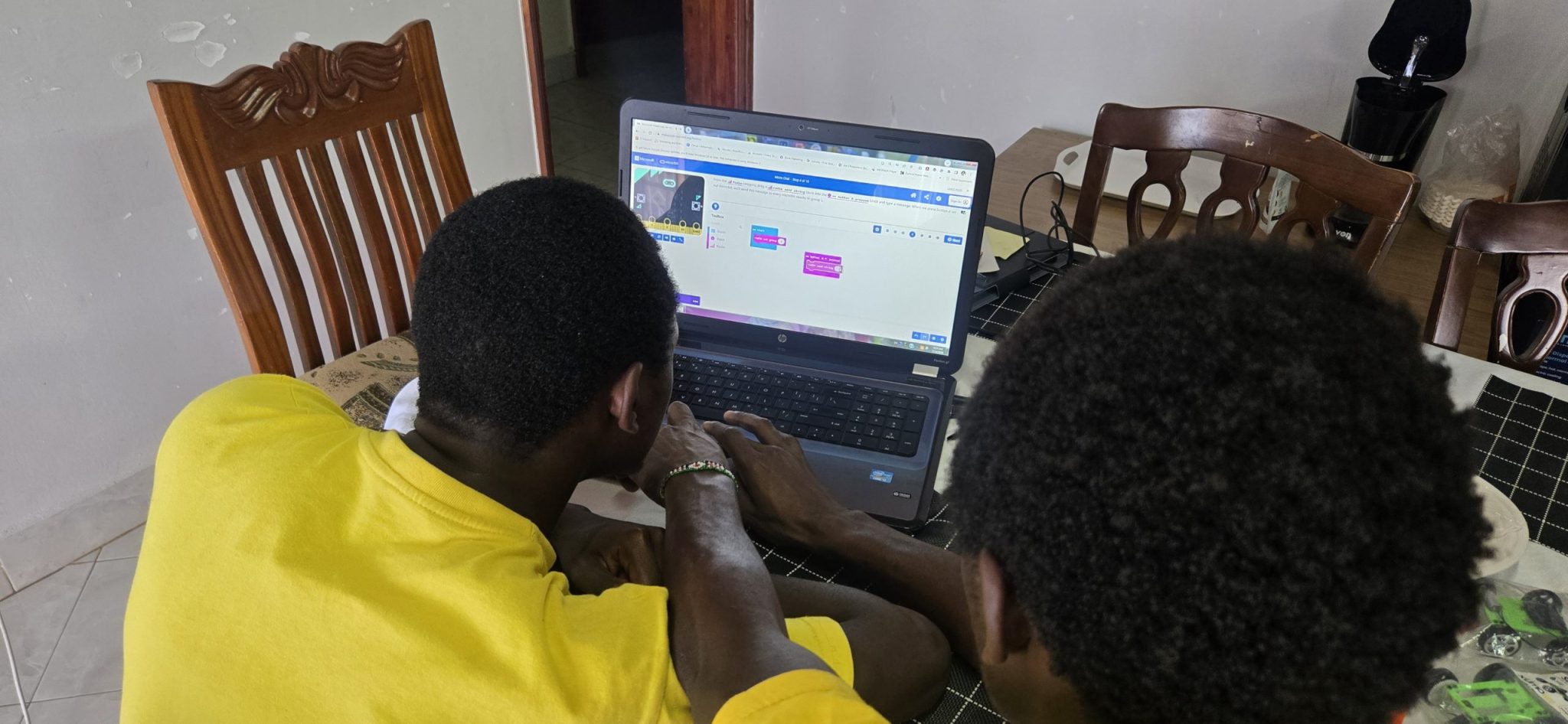 Two young men, Peter and Dominic, assembling small electronics and vehicle kits beside a laptop.