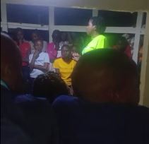 Children gathered under a gazebo listening to Kennesha speak during an evening activity.
